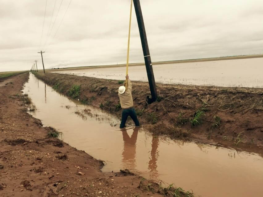 Leaning Power Pole and Lineman knee deep in mud and flood water for repairs