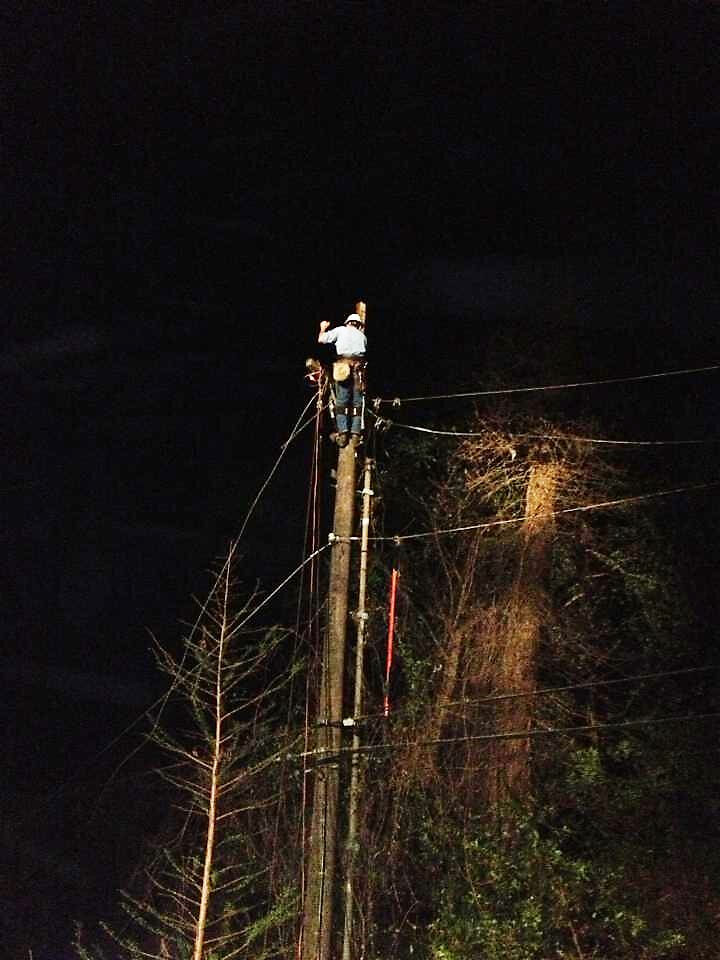 Lineman working by lights in the dark to repair high on power pole
